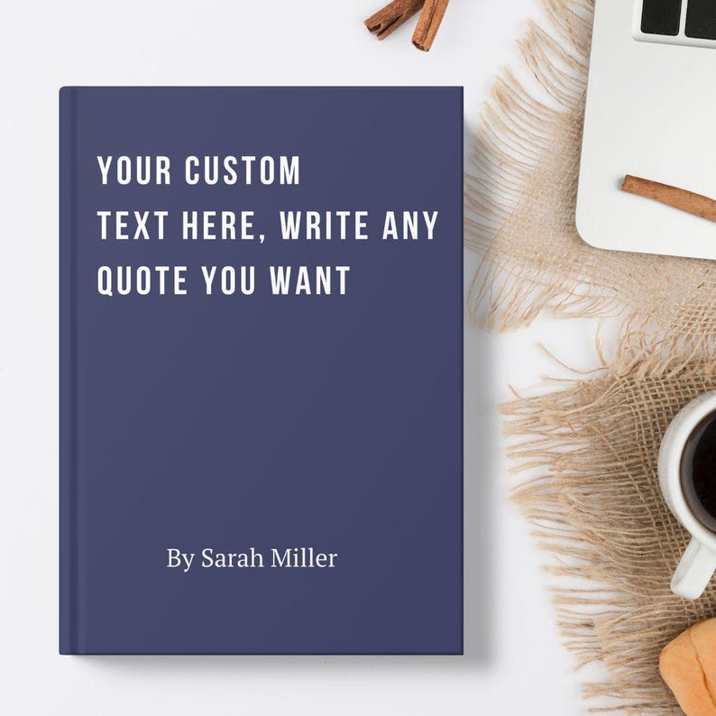 May include: A navy blue book with white text that reads "YOUR CUSTOM TEXT HERE, WRITE ANY QUOTE YOU WANT" and "By Sarah Miller". The book is on a white surface with a laptop and coffee cup.