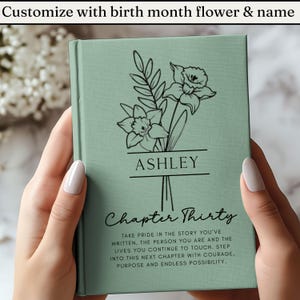 May include: A personalized sage green journal with a floral design and the name "ASHLEY" in black. The cover also features the words "Chapter Thirty" and inspirational text. The journal is held by a person.