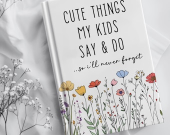 Könnte beinhalten: Ein weißes Hardcover-Notizbuch mit dem schwarzen Text CUTE THINGS MY KIDS SAY & DO ...so i'll never forget auf dem Einband, verziert mit einer bunten Illustration verschiedener Wildblumen in Rot, Gelb, Blau und Grün am unteren Rand.