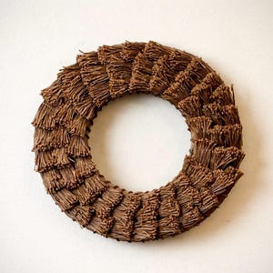 May include: A circular wreath made of brown twigs, arranged in layers to create a textured, layered effect. The wreath is a decorative item, suitable for seasonal or year-round display. The wreath is set against a plain white background.