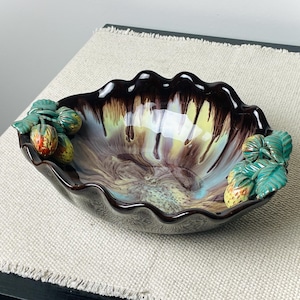 May include: A decorative ceramic bowl with a wavy rim and a glossy, dripped glaze in shades of brown, yellow, and blue. The bowl features green and yellow fruit and leaf accents on each side, adding a touch of nature-inspired design.