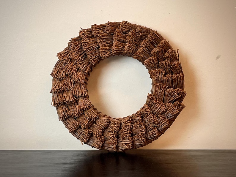 May include: A circular wreath made of brown twigs. The wreath is a decorative item, likely for seasonal or home decor. The twigs are arranged in a layered pattern, creating a textured, natural appearance. The wreath is displayed against a neutral background.
