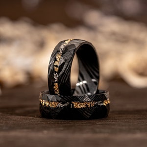 May include: Two black carbon fiber rings with gold inlay. The rings are stacked on top of each other.