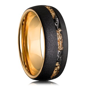 May include: A gold ring with a black textured band and a gold inlay. The ring's interior is polished gold. The inlay features gold and dark grey metallic elements, creating a striking contrast. The ring is a statement piece.