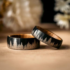 May include: Two black tungsten carbide rings with a wood inlay and a silver etched design of a forest.