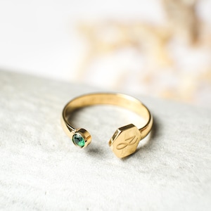 May include: Gold ring with a green gemstone and an infinity symbol on a hexagonal charm.
