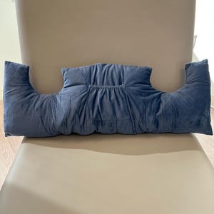 May include: A blue velvet pillow with armrests. The pillow is designed to provide support for the arms and neck while sitting.