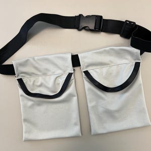 May include: A silver-colored utility belt with two pockets and a black adjustable strap with a buckle.