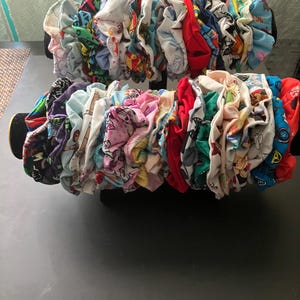 May include: A collection of colorful fabric scrunchies with various patterns and designs. The scrunchies are displayed on a black stand.