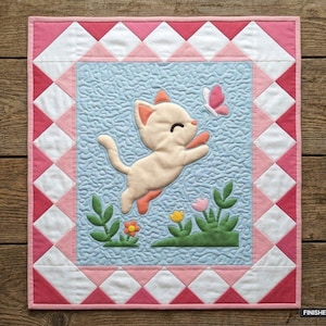 Op de afbeelding: Een rechthoekige quilt met een lichtblauw middenpaneel met een crèmekleurige kat die naar een roze vlinder springt. De rand bestaat uit roze en witte driehoeken. De quilt meet 91,44 cm bij 106,68 cm en bevat groene planten.