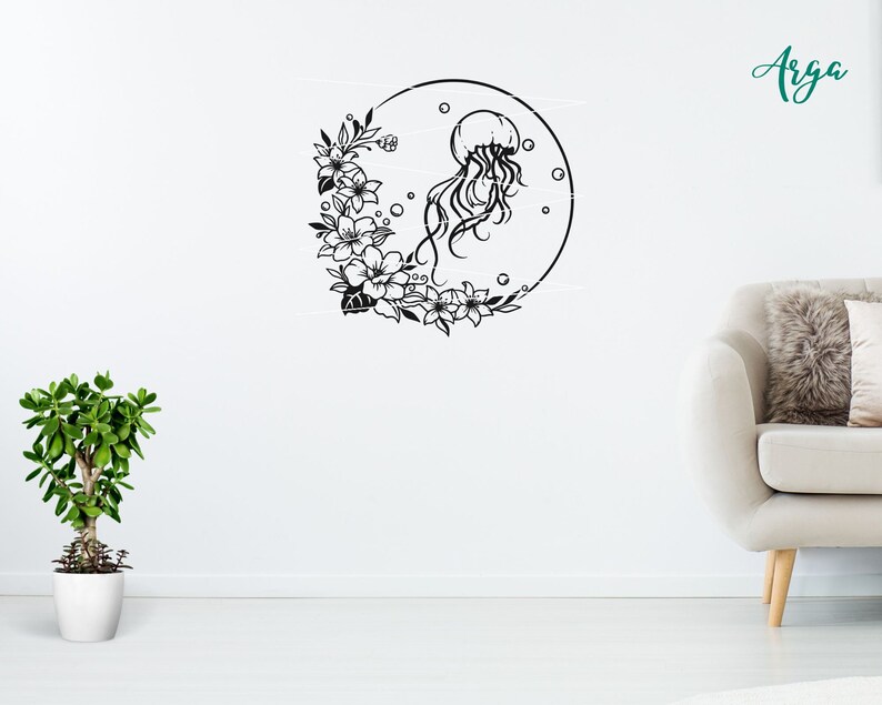 May include: Black and white silhouette of a jellyfish with floral accents in a circle. The design is on a white wall with a potted plant and a white couch in the background.