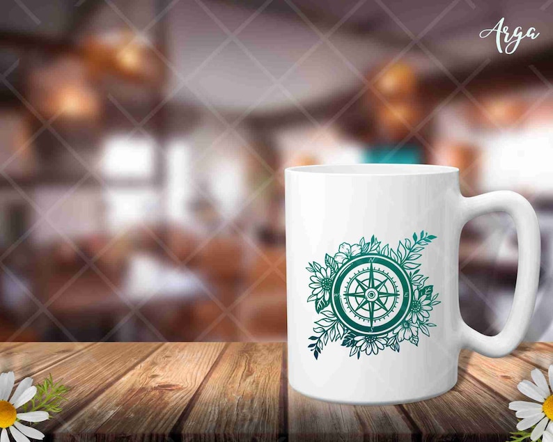 Peut inclure: Une tasse en c&eacute;ramique blanche avec un motif de boussole bleu sarcelle entour&eacute; de fleurs. La boussole a quatre points et est entour&eacute;e d'une couronne de fleurs.