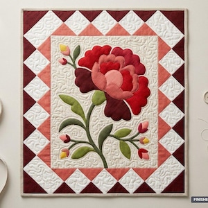 Puede incluir: Una colcha rectangular con una gran flor central roja y rosa con hojas verdes sobre un fondo crema. El borde consiste en un patrón de diamantes en blanco, coral y rojo oscuro. El tamaño final es de 91,44 cm por 106,68 cm.