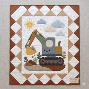 Op de afbeelding: Een rechthoekige quilt met een centrale applicatie van een grijze en groene graafmachine met een gele bak, een lachende zon en blauwe wolken. De rand heeft bruine en witte driehoeken. Een label in de hoek vermeldt Finished Size: 36"x42".