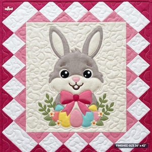 May include: A quilted wall hanging featuring a central gray bunny with a pink bow, surrounded by colorful Easter eggs and green foliage. The border consists of a diamond pattern in shades of pink and white. The text reads: FINISHED SIZE 36" x 42".