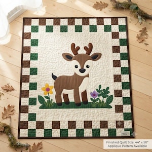 May include: A rectangular quilt featuring a central applique of a brown deer with antlers standing on green grass with yellow and purple flowers. The quilt has a cream-colored background with a checkered border of brown and green squares. Text reads 44" x 50".