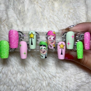 Puede incluir: Conjunto de diez uñas postizas con varios diseños que representan personajes de la caricatura Los Padrinos Mágicos. Los diseños incluyen purpurina verde y rosa, una uña rosa con una estrella dorada, una uña verde con una caricatura de Timmy Turner, una uña rosa con una caricatura de Cosmo y una uña verde con una caricatura de Wanda.