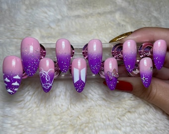 May include: Set of ten purple and pink ombre press-on nails with various white designs, including clouds, a heart, a butterfly, and the letters "BT" in a stylised font.