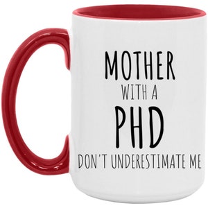Op de afbeelding: Witte keramische koffiemok met een rode rand en handvat. De mok heeft zwarte tekst met de tekst "Moeder met een PhD Onderschat me niet."