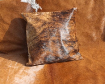 May include: A brown and white cowhide cushion with a soft, plush texture. The cushion is made from real cowhide and has a unique, natural pattern.