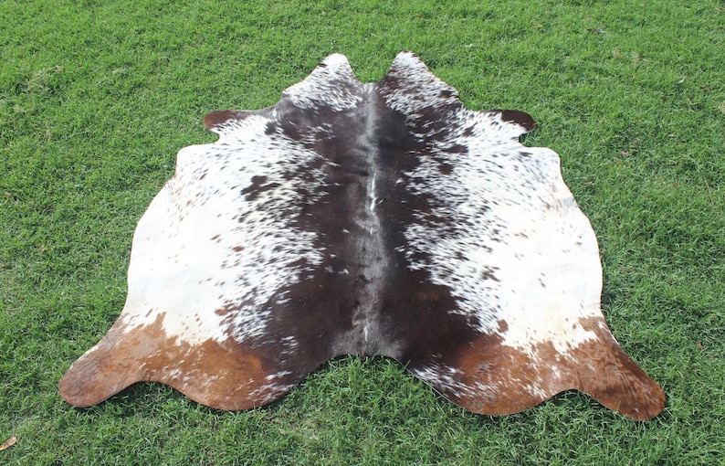 Puede incluir: Una alfombra de piel de vaca marr&oacute;n y blanca con un patr&oacute;n natural. La alfombra est&aacute; doblada por la mitad y tiene una combinaci&oacute;n de colores marr&oacute;n, blanco y tostado.