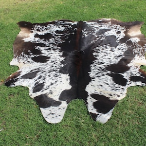 Puede incluir: Una alfombra de piel de vaca negra y blanca con un patr&oacute;n de manchas. La alfombra est&aacute; hecha de cuero natural y tiene un aspecto r&uacute;stico.