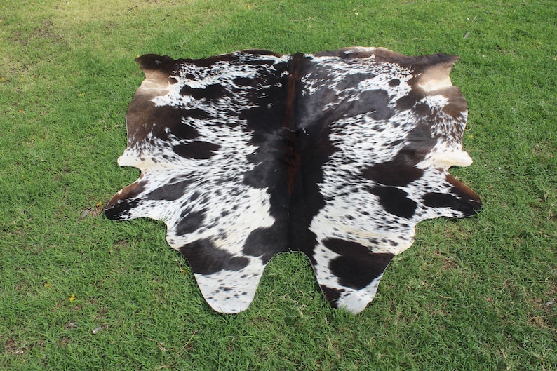 Puede incluir: Una alfombra de piel de vaca negra y blanca con un patr&oacute;n de manchas. La alfombra est&aacute; hecha de cuero natural y tiene un aspecto r&uacute;stico.