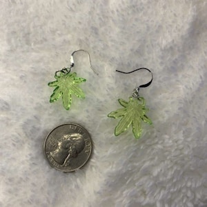 Peut inclure: Une paire de boucles d'oreilles en forme de feuille vert clair avec des crochets argentés. Une pièce de monnaie américaine est à côté des boucles d'oreilles pour la comparaison de taille. Les boucles d'oreilles sont en matériau translucide.