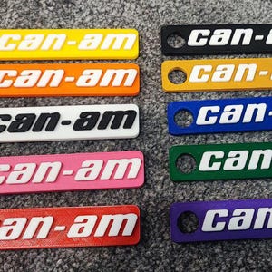 May include: Ten keychains with the text "can-am" in various colors, including yellow, orange, white, pink, red, green, blue, and purple.