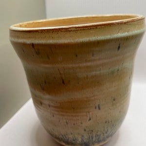May include: A brown ceramic planter with a white glaze and black speckles. The planter has a rounded bottom and a wide opening.