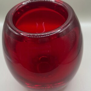 May include: A deep red glass candle holder with a rounded, oval form. The thick glass has a glossy finish, and the opening is wide. The candle holder is designed to hold a single candle. The overall design is modern and minimalist.