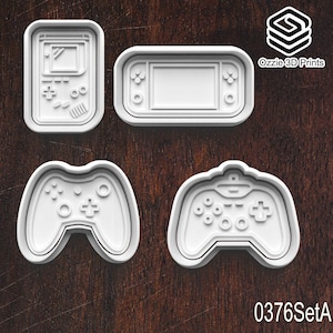 May include: Four white plastic cookie cutters shaped like retro video game controllers and handheld consoles. The set includes a classic handheld, a modern handheld, and two controller designs. The text "0376SetA" is visible.
