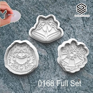 May include: Three white Christmas-themed cookie cutters. The cutters feature bell and wreath designs. The text "0168 Full Set" is at the bottom of the image. The cookie cutters are being held by a person.