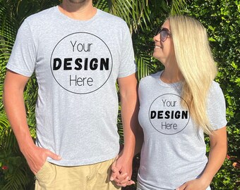 May include: A couple wearing matching gray t-shirts with the text "Your Design Here" in a circle on the front. The man is wearing khaki shorts and the woman is wearing denim shorts.