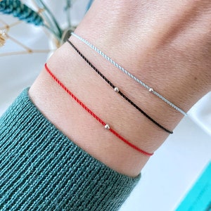 May include: Three string bracelets with silver beads. The bracelets are red, black, and light blue.