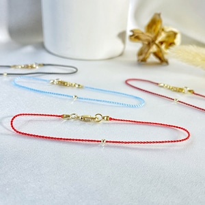 Puede incluir: Cuatro pulseras con cierres y cuentas doradas. Las pulseras son roja, azul claro, azul oscuro y gris.