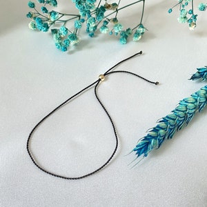 Puede incluir: Un brazalete ajustable simple negro con un pequeño acento de cuentas doradas.