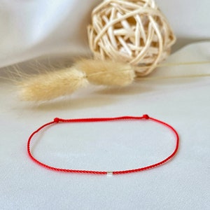 May include: A red string bracelet with a small silver bead.