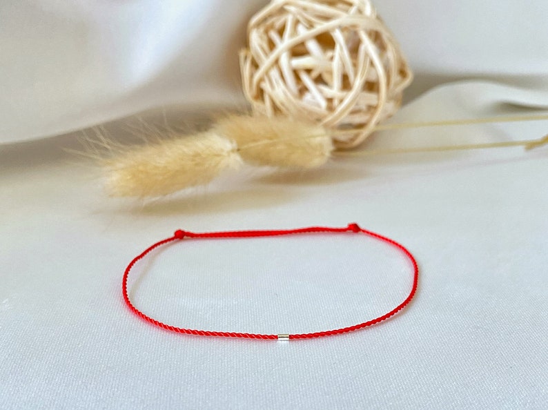 May include: A red string bracelet with a small silver bead.