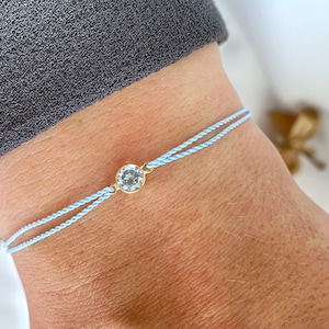 Peut inclure: Un bracelet en cordon bleu clair avec un charme en cristal transparent. Le charme est serti d'or.