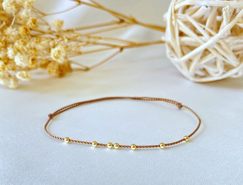 May include: A brown string bracelet with five gold beads.