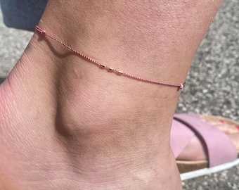 May include: A pink ankle bracelet with small gold beads. The bracelet is worn on a person's ankle.