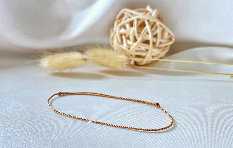 May include: A brown braided cord bracelet with a silver bead accent.
