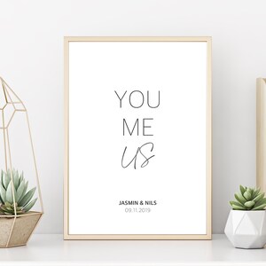 Könnte beinhalten: Ein gerahmter Druck mit den Worten "YOU ME US" in einer minimalistischen Schriftart. Unter dem Text steht "JASMINE & NILS 09.11.2019".