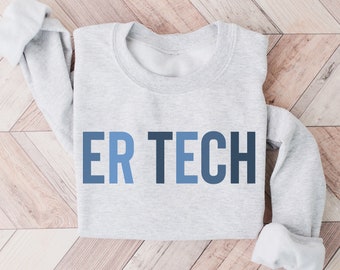 May include: A light gray sweatshirt with the text "ER TECH" in shades of blue. The sweatshirt is displayed on a light wood-grain surface. The sleeves are rolled up.