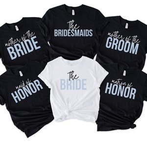 May include: Six black and white t-shirts with different text in blue and white. The text on the shirts reads: "mother of the bride", "maid of honor", "matron of honor", "the bridesmaids", "mother of the groom", and "the bride".