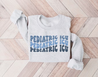 Puede incluir: Una sudadera gris con el texto "PEDIATRIC ICU" repetido tres veces en una fuente degradada azul y blanca.