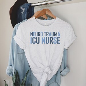 May include: A white t-shirt with the text "Neuro Trauma ICU Nurse" in blue and gray lettering.