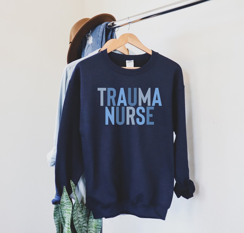 May include: A navy blue sweatshirt with the text "TRAUMA NURSE" printed in blue and gray ombre lettering.