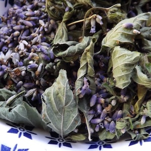 May include: A bowl filled with dried lavender flowers and green leaves. The bowl has a blue and white pattern.